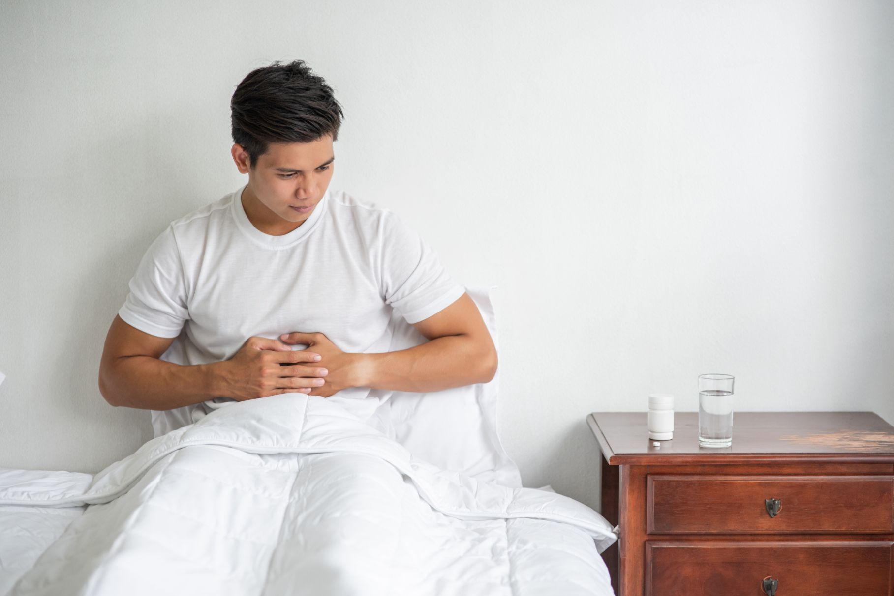 A man sits in bed with a stomachache and presses his stomach with his hands